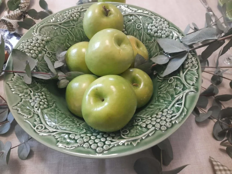 Balanced table composition with English dinnerware, silver flatware, green apples, eucalyptus and textured green glassware