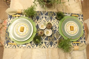 Blue and green table setting with layered dinnerware, rosemary plants and textured green glassware for elegant everyday dining