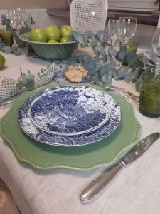 Layered place setting with English porcelain, silver flatware and green glassware.
