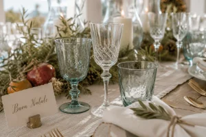 Blue and clear crystal glassware paired with artisan dinnerware on a coastal Mediterranean Christmas table with natural greenery and candlelight.